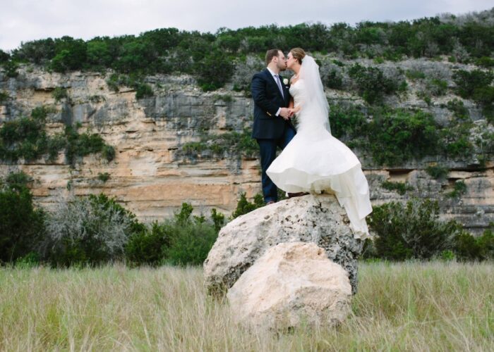 Wedding couple kissing on rock with cliff backdrop